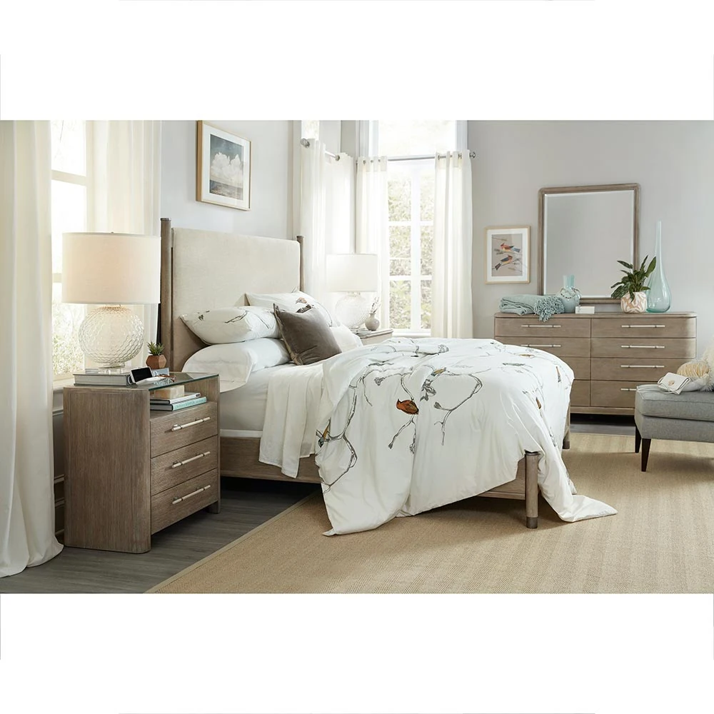 A bedroom with a light brown wooden dresser, a bed, and a nightstand.
