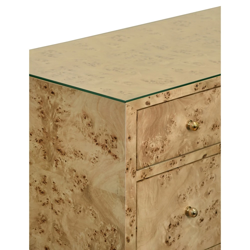 A close-up of the corner of a dresser with a light-colored wood finish and gold knobs