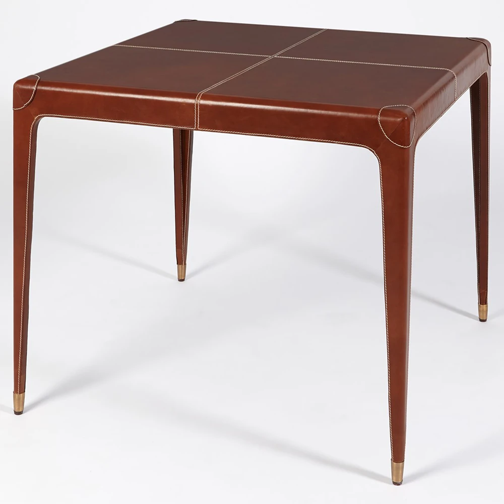 An angled view of a brown leather table with four legs and white stitching.