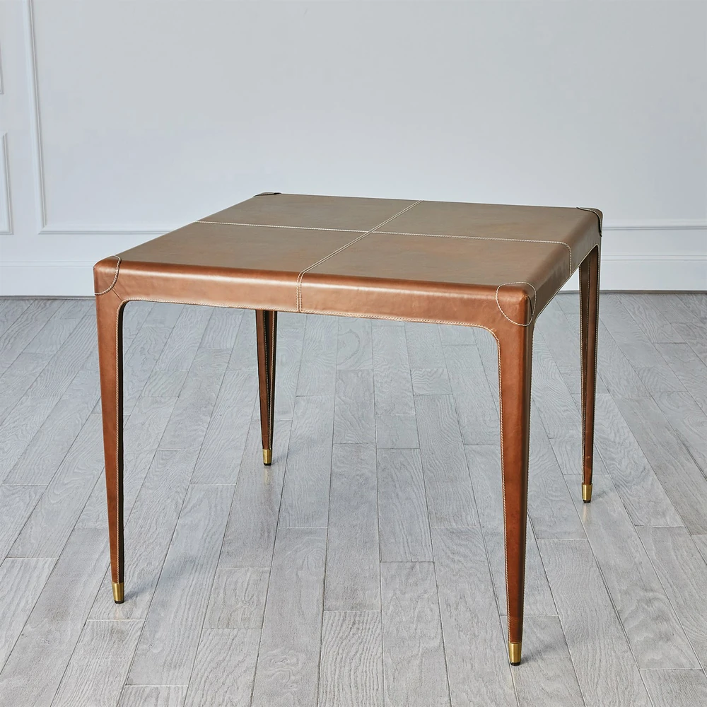 A brown leather table with four legs and white stitching in a room with a wooden floor from another angle.