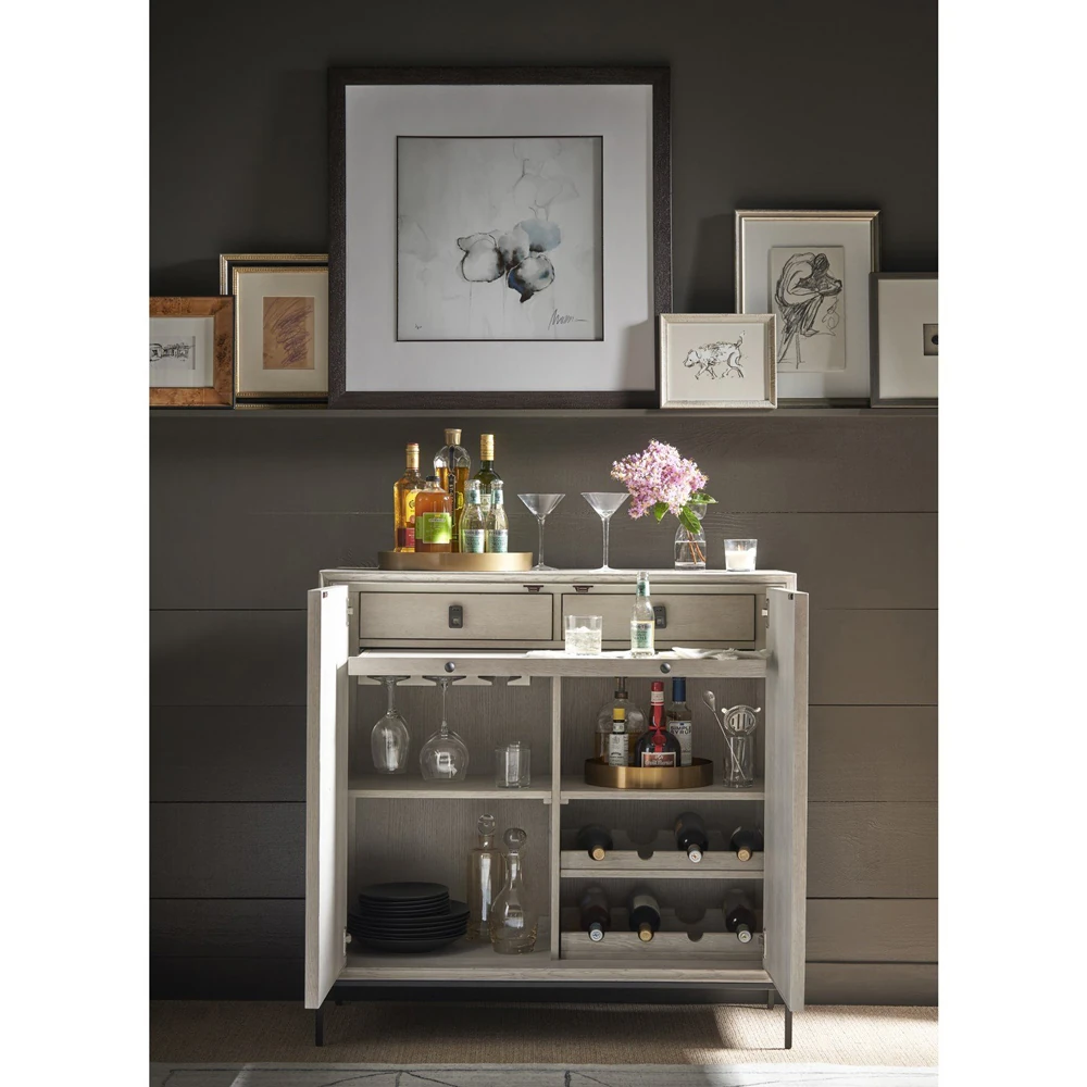 A beige cabinet with two drawers and open shelves, stocked with wine and glasses.