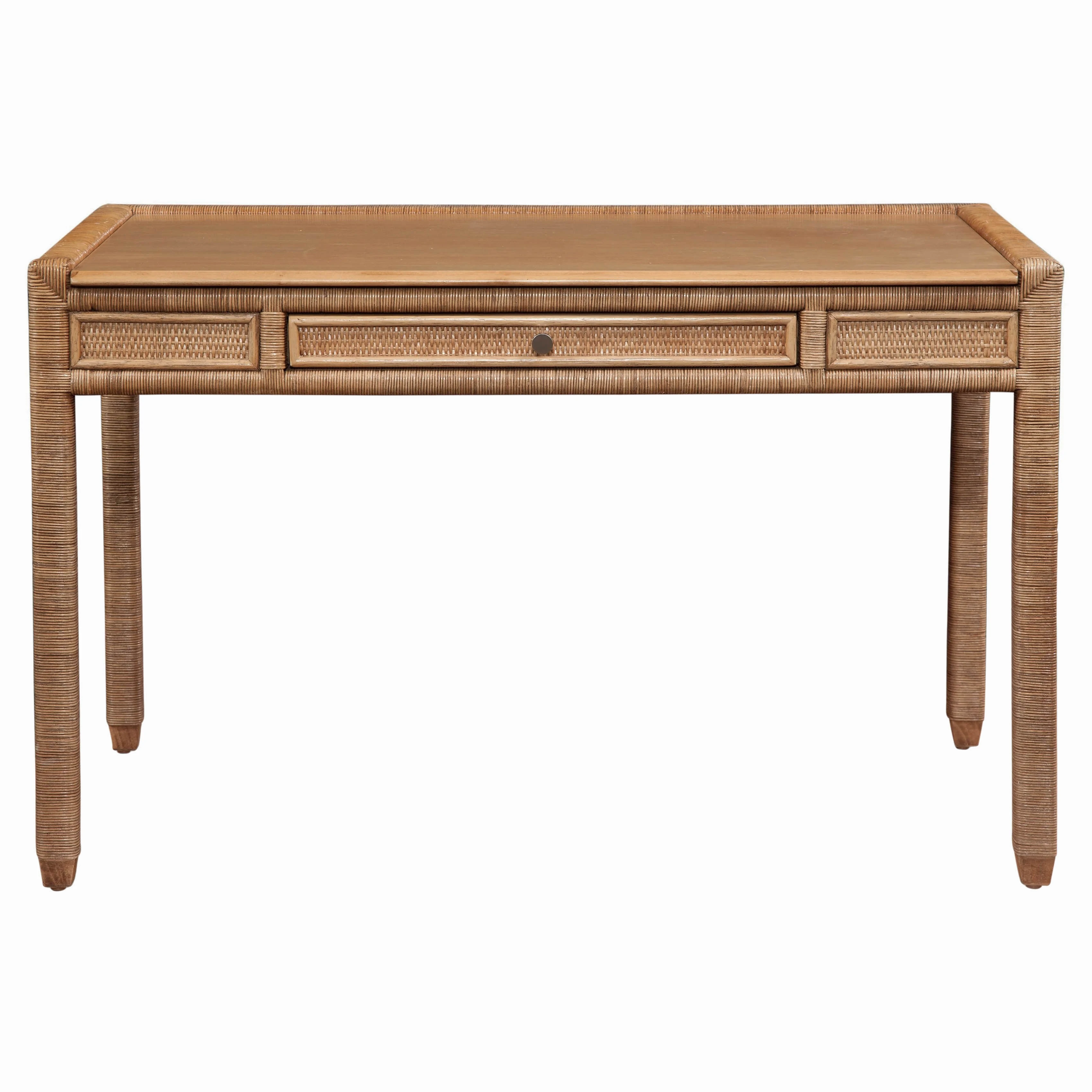 A rectangular desk with a light brown wooden top and a wicker frame, featuring three drawers.